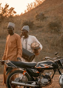 Two traditional musicians with drums and a motorcycle in Zaria City, Nigeria.
