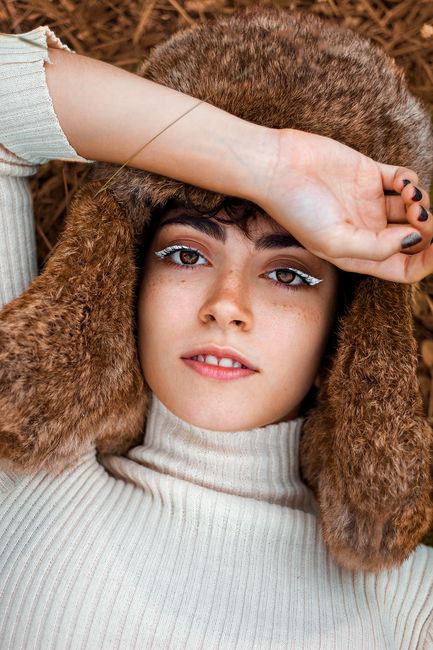 Stylish portrait of a woman with bold makeup wearing a fur hat and sweater.