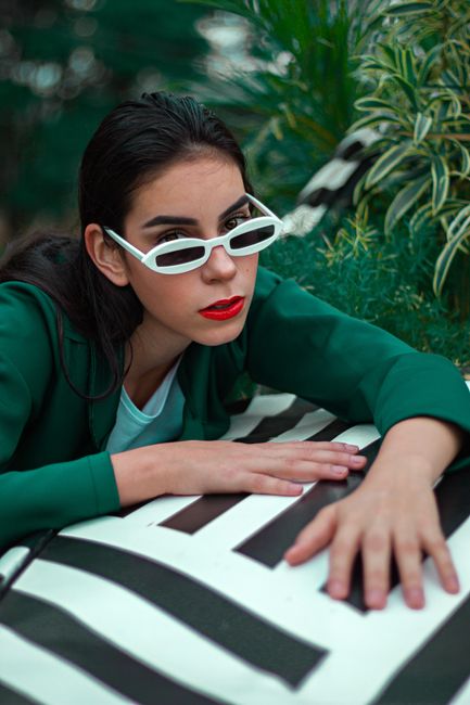 Stylish woman with sunglasses poses over a striped cushion, expressing modern fashion outdoors.