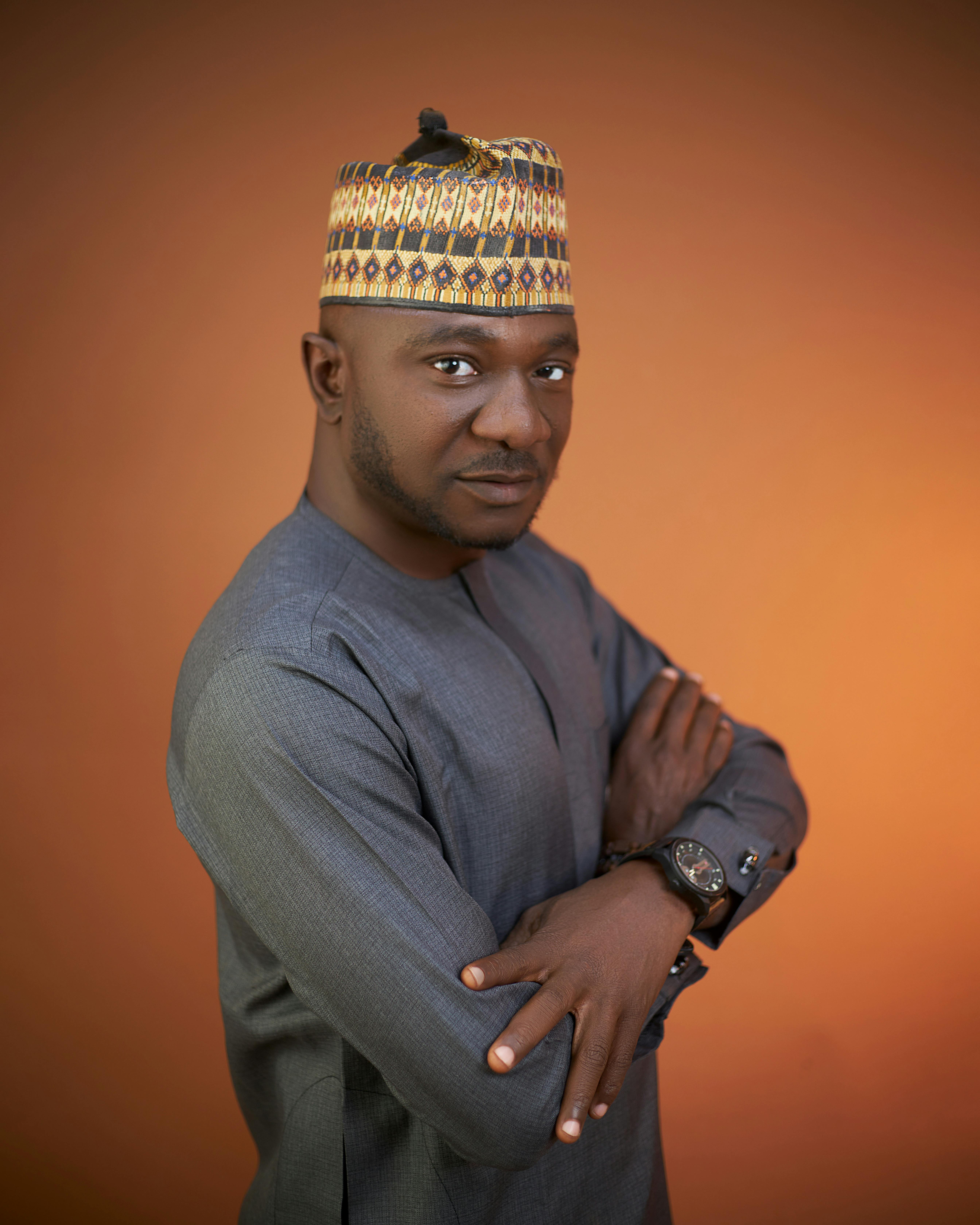 Portrait of a confident African man in traditional attire with an orange background.