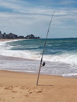 A solitary fishing rod stands on the sandy beach overlooking the ocean in Macaé, Brazil.