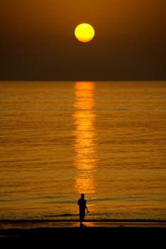 Serene sunrise on As Sifah Beach, Oman with a lone silhouette reflecting against the ocean.