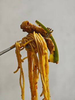 Delicious forkful of spaghetti with green peppers and slices of meat against a plain background.