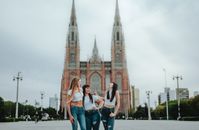 Three women share a joyful moment in front of the iconic La Plata Cathedral, Argentina.