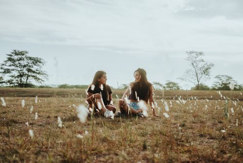 Free Two young women enjoy a serene moment sitting in a grassy field during summer. Stock Photo