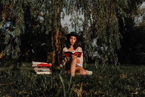 Free A young woman enjoying a book beneath a tree in a serene park setting. Stock Photo
