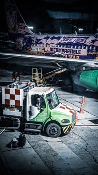 Night scene of airplane refueling at an airport with colorful graphics.