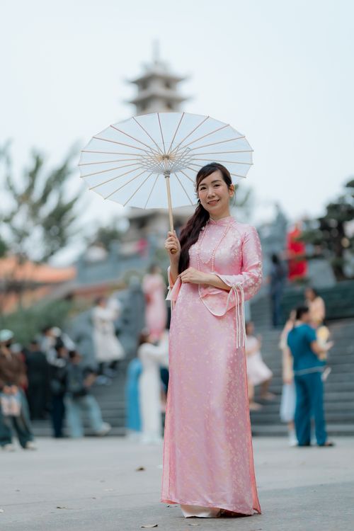 Free Elegant woman in traditional pink dress holding a parasol in an outdoor setting with blurred people in background. Stock Photo