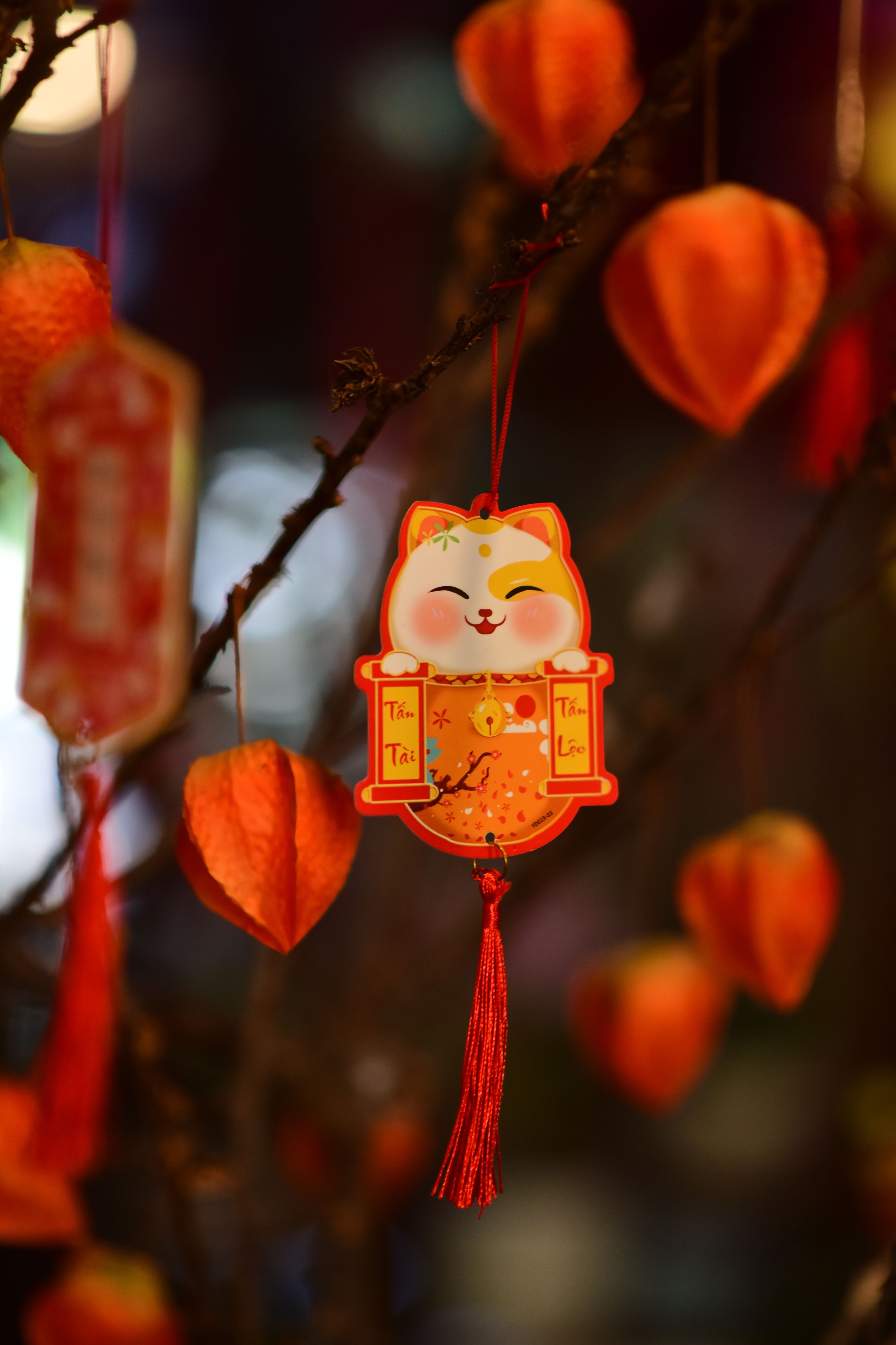 Close-up of a colorful Maneki-neko decoration on a branch for Chinese New Year celebration.