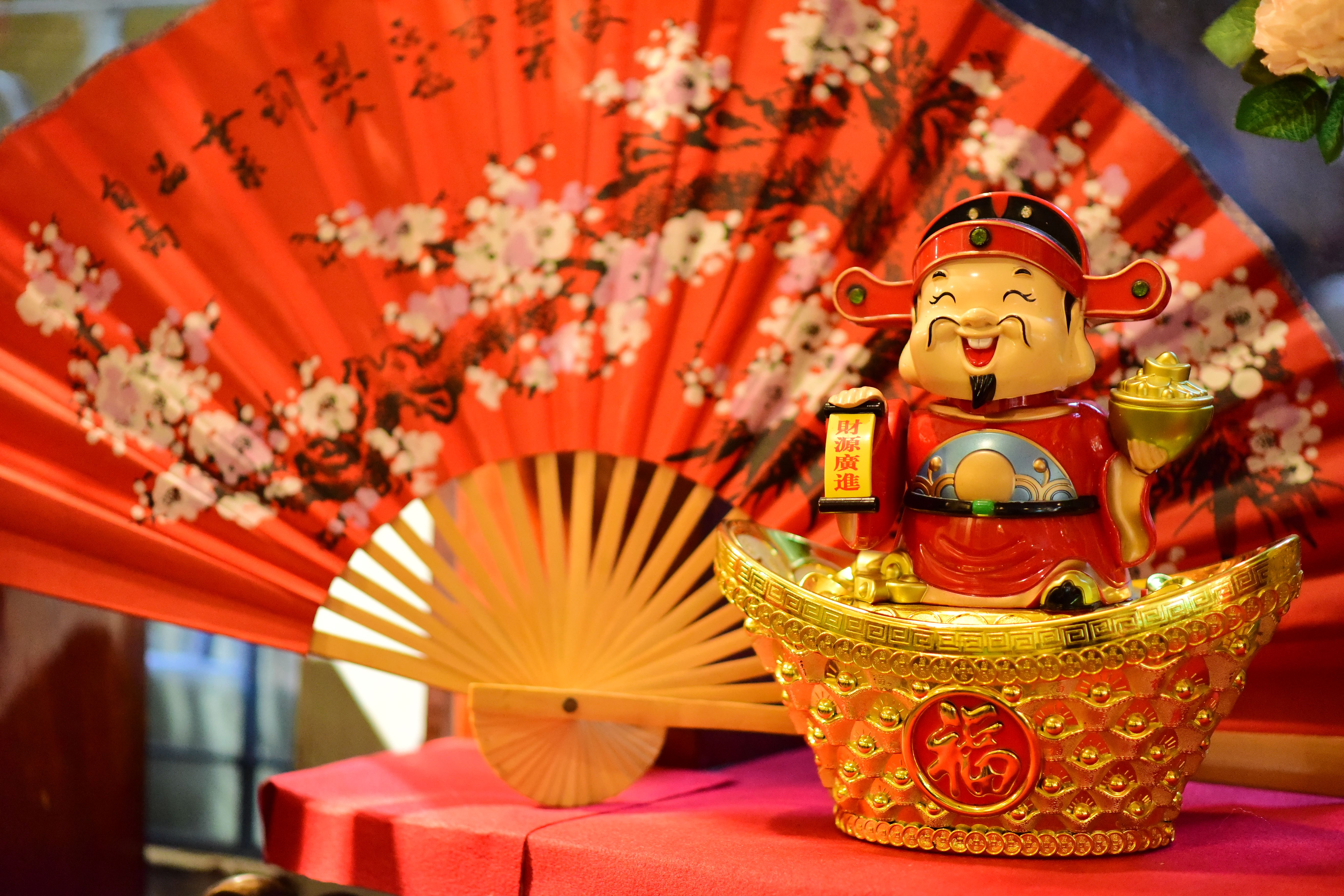 Vibrant image of a Chinese good luck figurine with a red decorative fan, symbolizing prosperity.