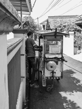 Black and white photo of a street vendor pushing a cart in a narrow urban alley.