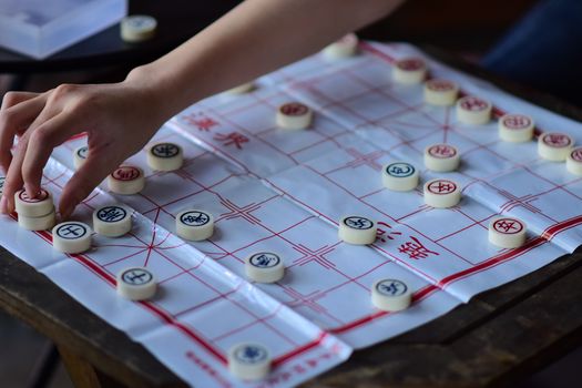 A hand strategically moves a piece on a Chinese chess board, showcasing traditional strategy game play.