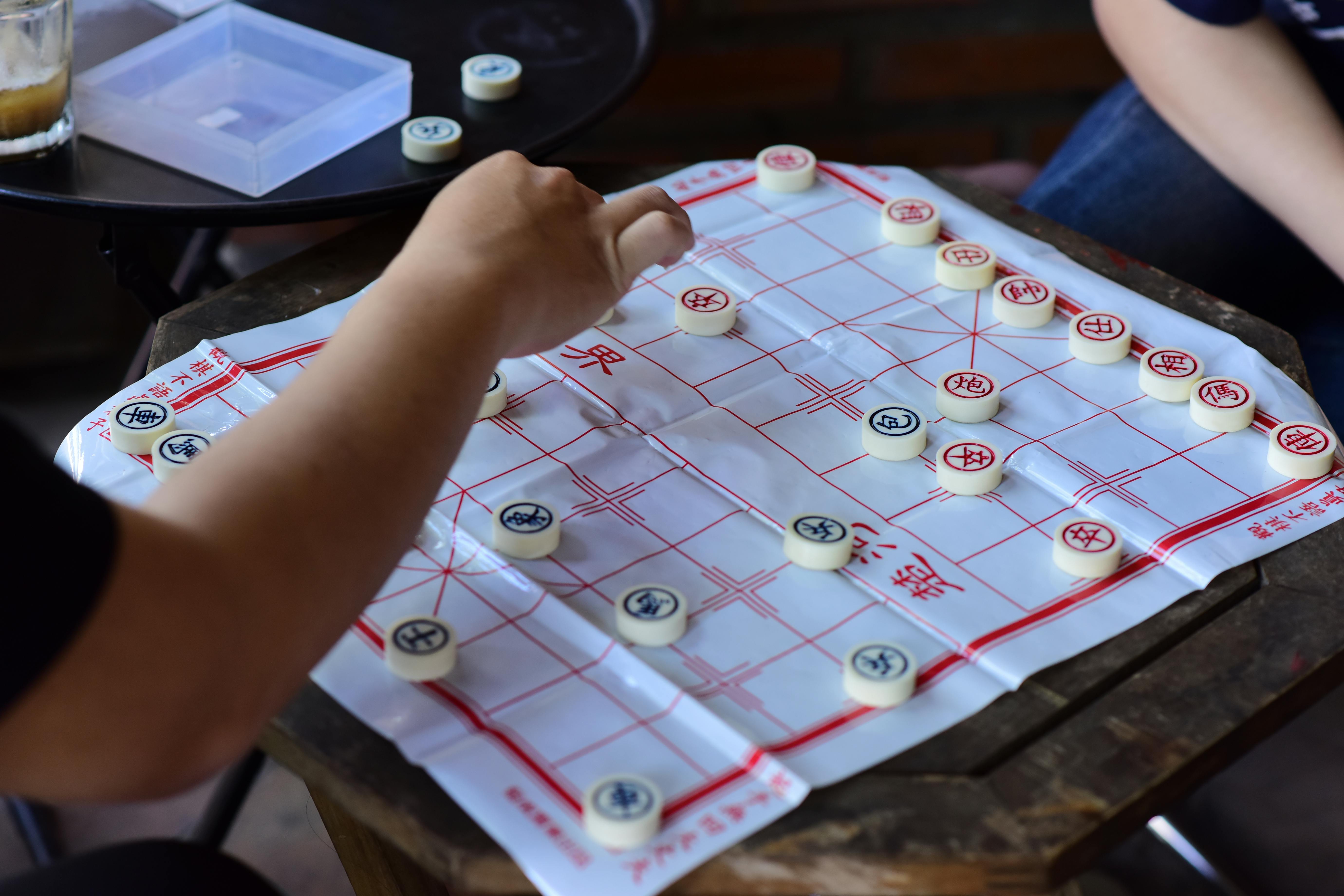Two individuals engaged in a strategic game of Chinese chess at a table indoors.