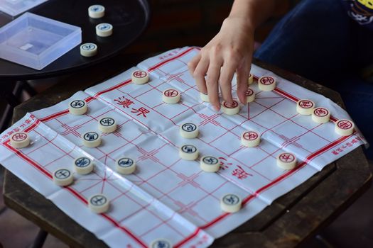 A person strategically plays Chinese chess, making a move on a board with clear text visible.