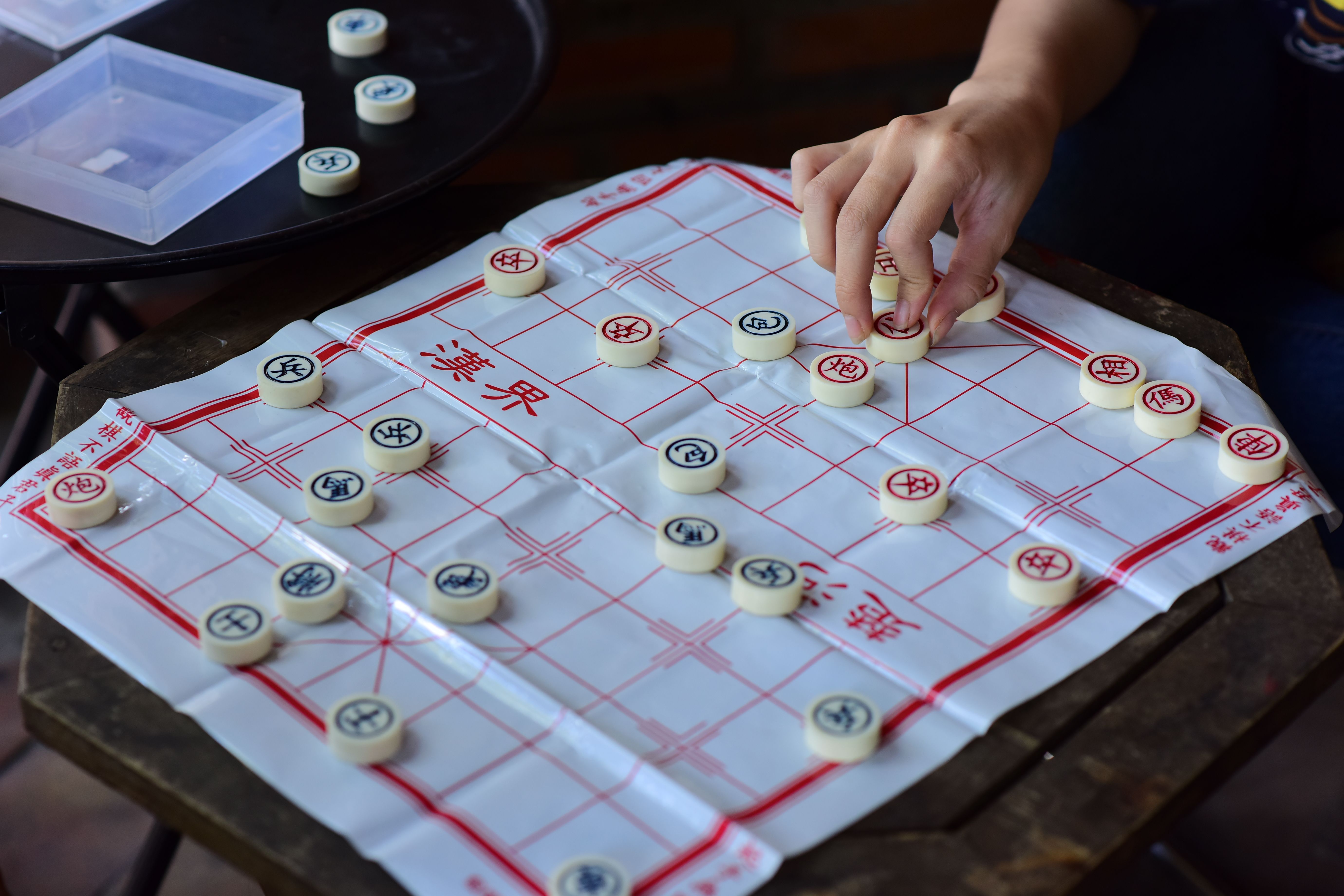 Close-up of a person playing Chinese chess with strategic skills on a wooden table.