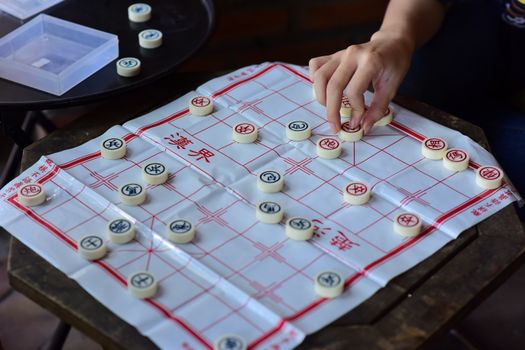 Close-up of a person playing Chinese chess with strategic skills on a wooden table.