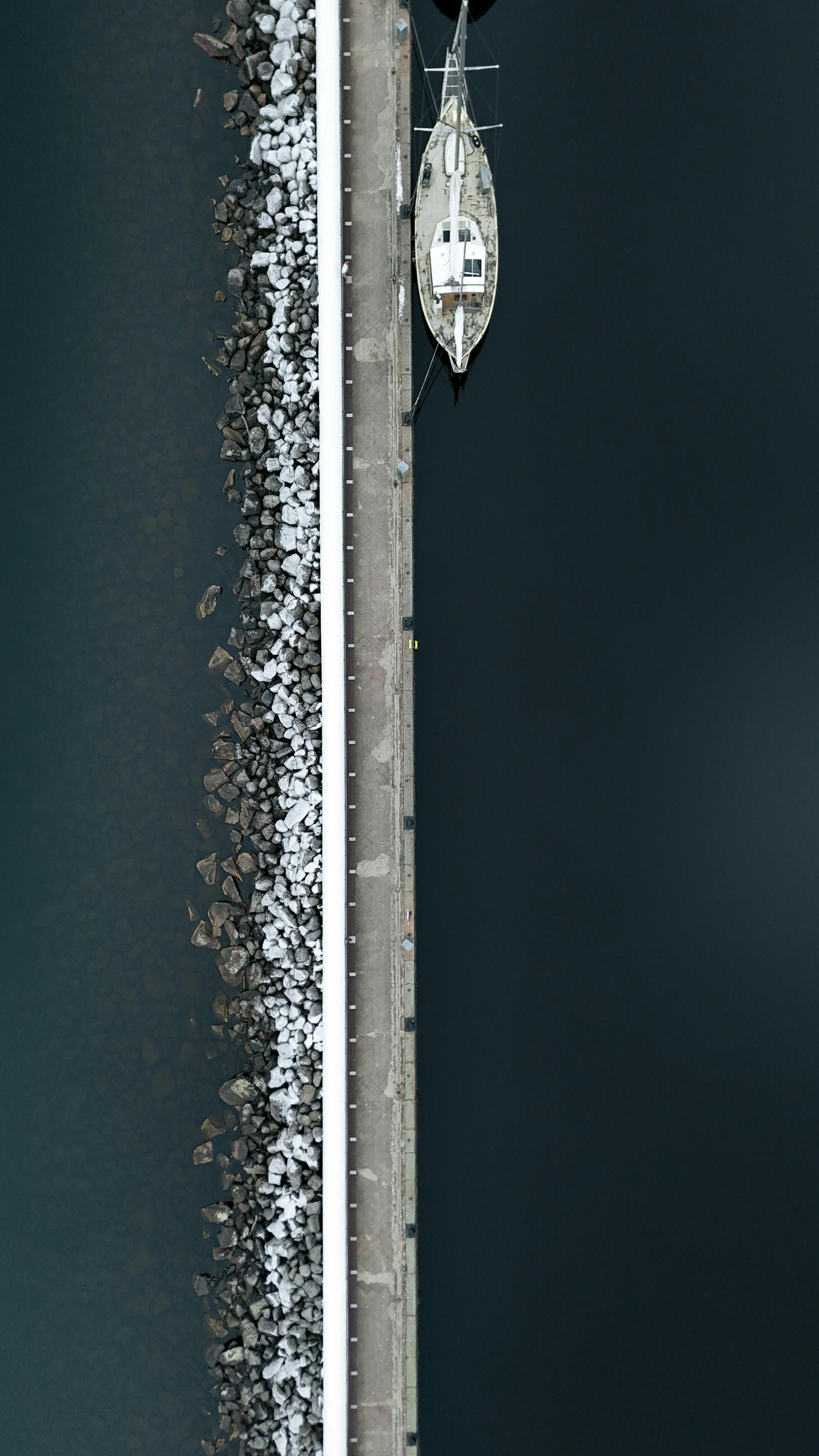 Bezpłatne Ujęcie lotnicze żaglówki zacumowanej przy skalistym nabrzeżu w Jönköping, ukazujące symetrię i spokojne wody. Zdjęcie z galerii