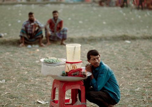 Street vendor selling snacks outdoors. Two men sitting in background.