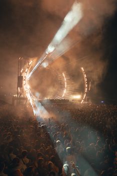 A large crowd enjoys a nighttime music festival with spectacular lights and stage design.