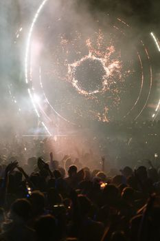 Lively crowd enjoying a vibrant music festival with dynamic light show at night.