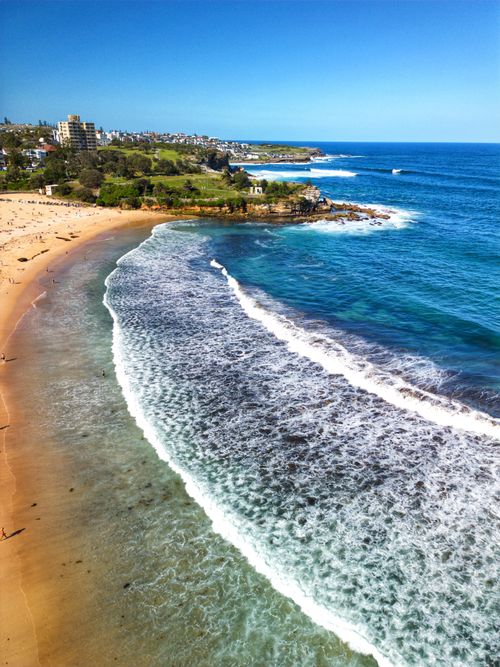 Free Stunning aerial view of a beautiful beach with clear blue waters and gentle waves under a sunny sky. Stock Photo