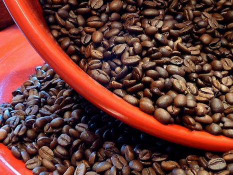 Close-up of roasted coffee beans spilling from a red bowl, showcasing rich textures and vibrant colors.