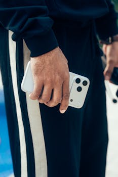 Close-up of a person holding a modern smartphone, showcasing casual streetwear style outdoors.