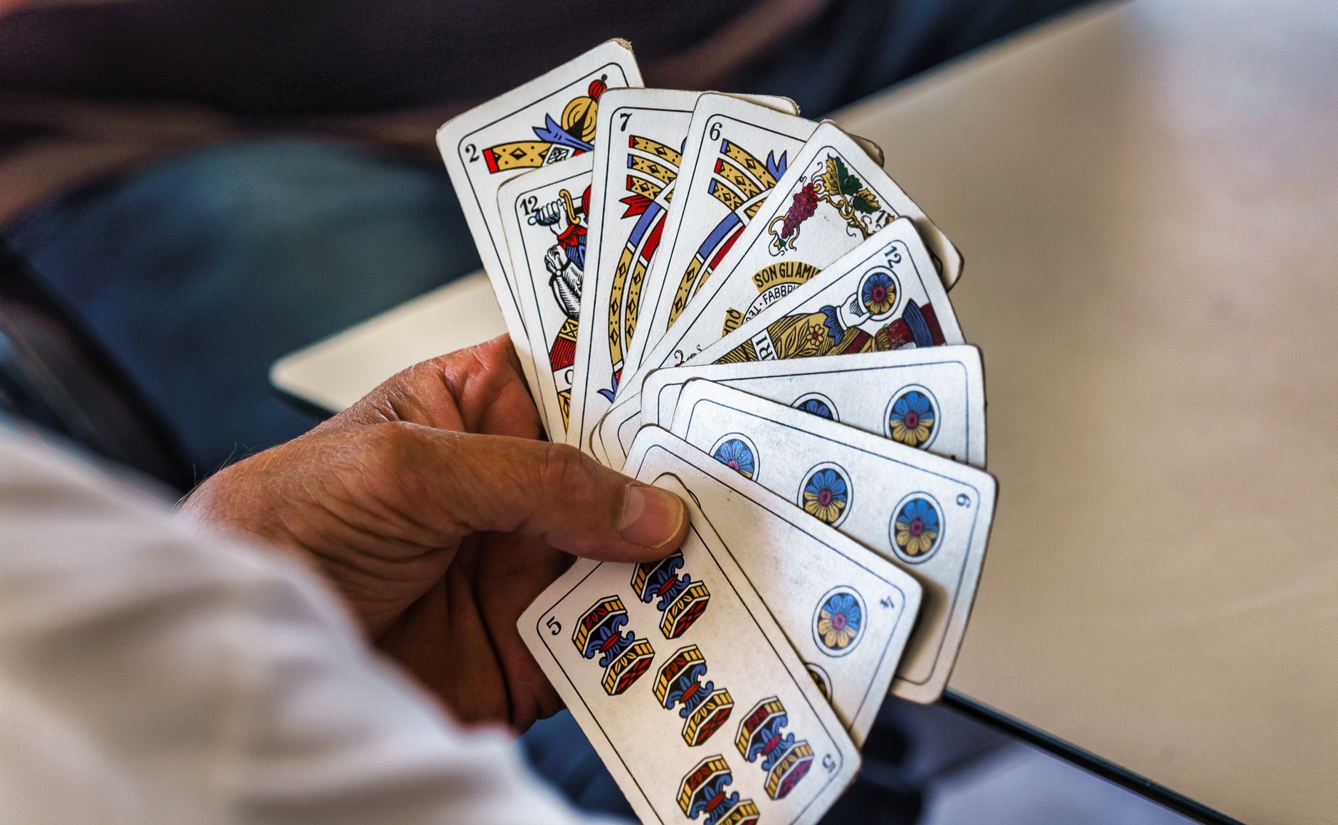 Close-up of a hand holding a fan of traditional Briscola playing cards.
