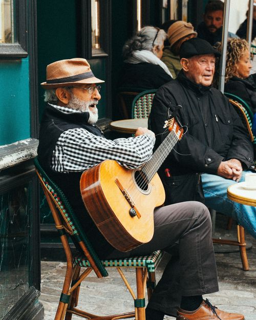 Free Senior man playing guitar at a street cafe, enjoying a relaxed afternoon. Urban lifestyle captured. Stock Photo