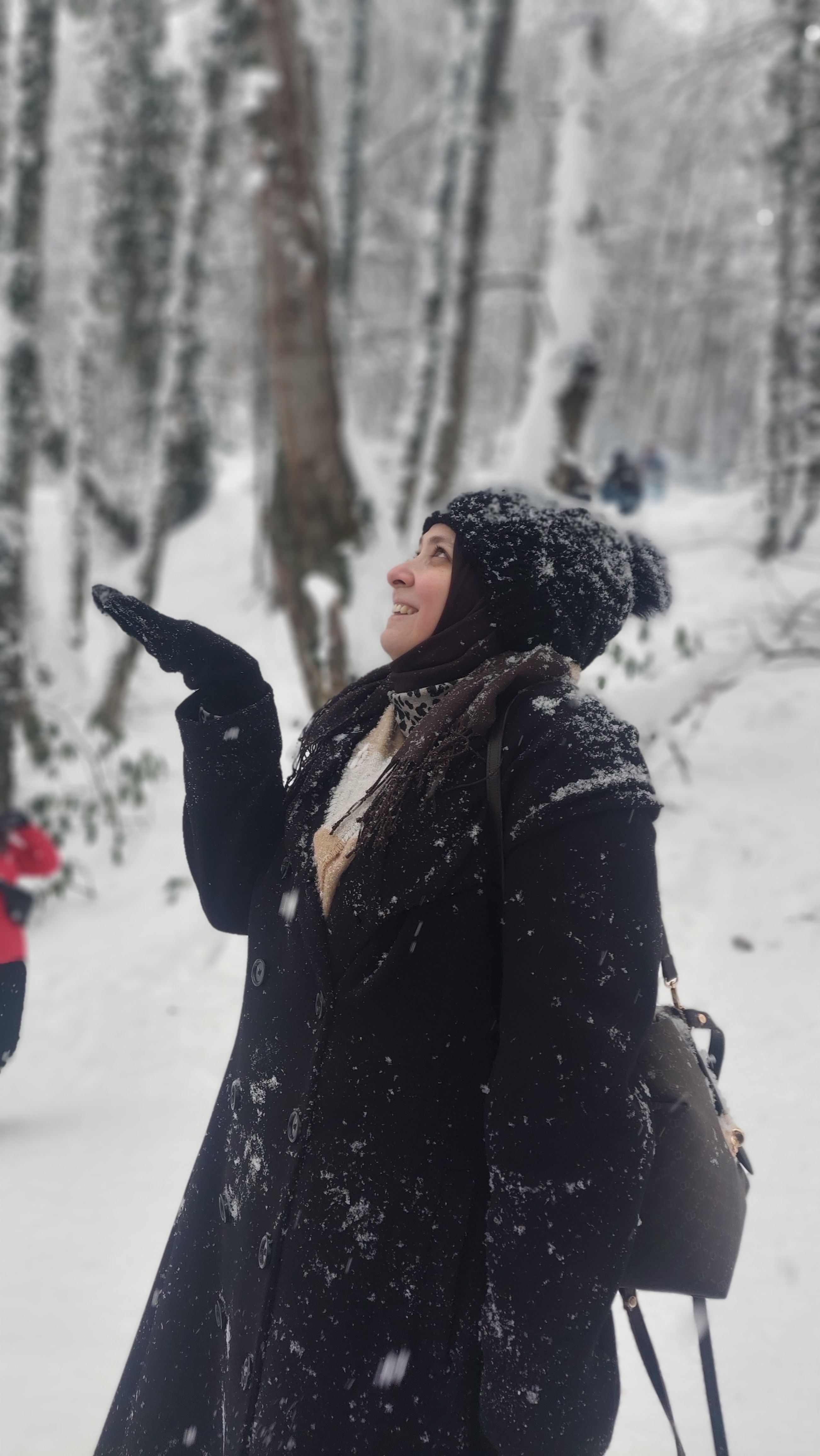 Woman in a snowy forest wearing winter clothes, enjoying the snowfall.