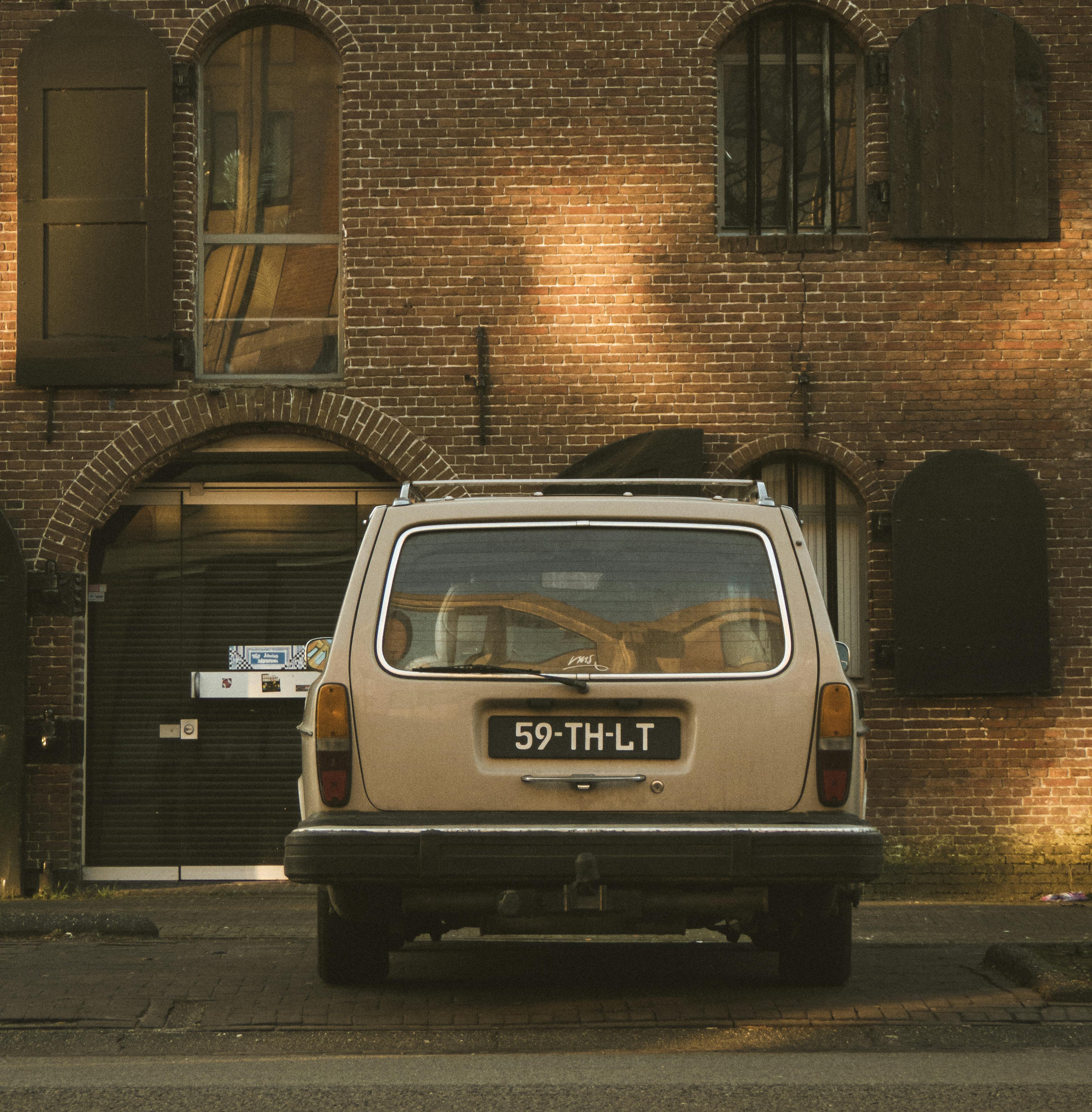 Rear view of a vintage car parked in front of a rustic brick building with arched windows.