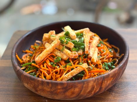 Close-up of savory Schezwan noodles topped with crispy paneer in a wooden bowl, perfect for Asian cuisine enthusiasts.