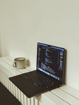 Open laptop displaying code in a minimalist workspace next to a cup, perfect for tech or home office themes.