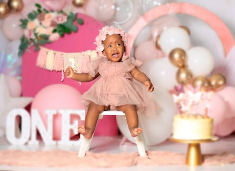 Cute baby girl celebrates her first birthday with a pink-themed party setting.