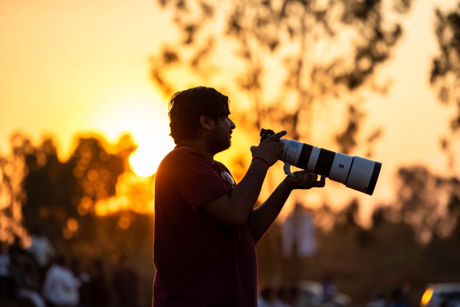 Fotógrafo usando teleconversor com objetiva longa em campo aberto durante hora dourada