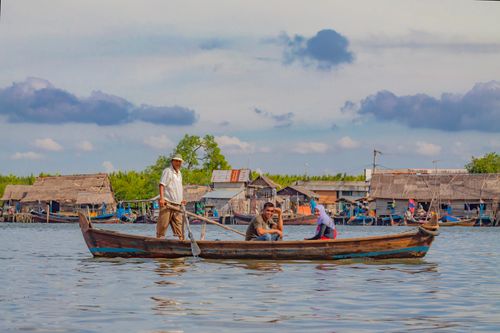 Free A wooden boat on calm waters in Indonesia's North Sumatra, with traditional village in the background. Stock Photo