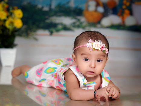 Adorable baby girl posed indoors in a floral dress with soft pastel tones.