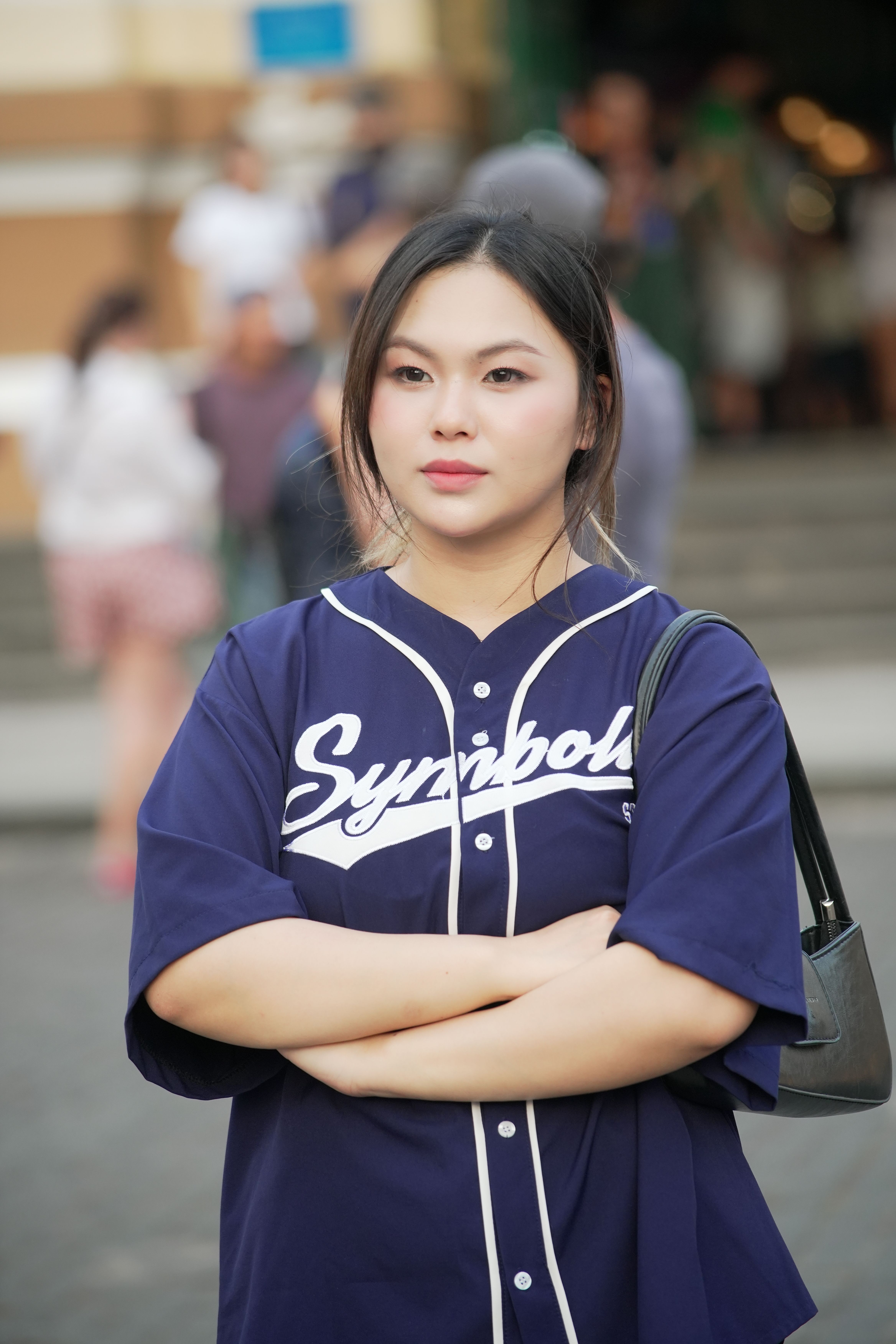 Young woman in blue casual outfit standing confidently with arms crossed outdoors.