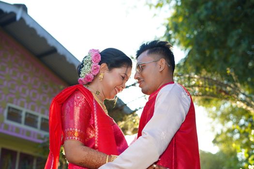 A happy Indian couple in vibrant traditional attire celebrating their wedding outdoors.