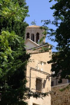 Old stone church tower peeking through lush green trees under a clear blue sky.