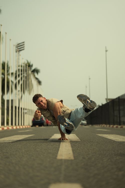 Free Street dancer performing acrobatic breakdance on an empty road in Togo amidst lined flagpoles. Stock Photo