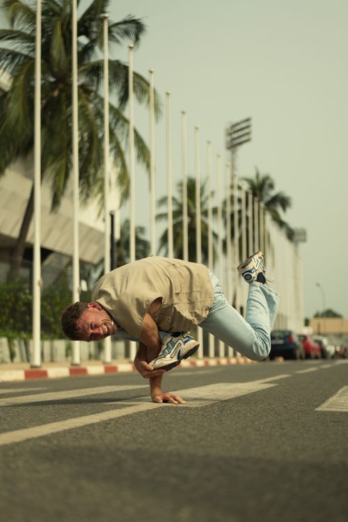 Free Breakdancer skillfully performing on a sunny street in Togo with palm trees in background. Stock Photo