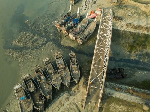 Free Aerial shot of boats moored by a riverbank, showcasing a rustic and industrial landscape. Stock Photo