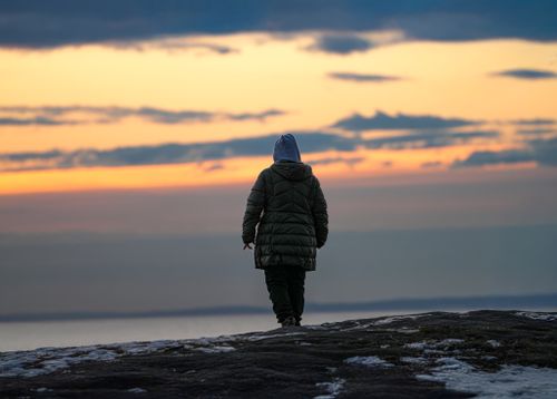 Free A lone figure in winter clothing walking on a snowy beach at sunset. Stock Photo