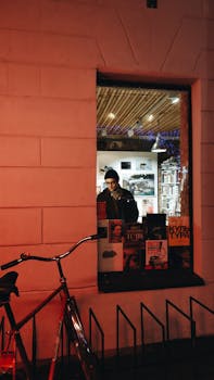 A man views books through a lit window in Sankt-Peterburg, Russia. Bicycle outside creates urban charm.