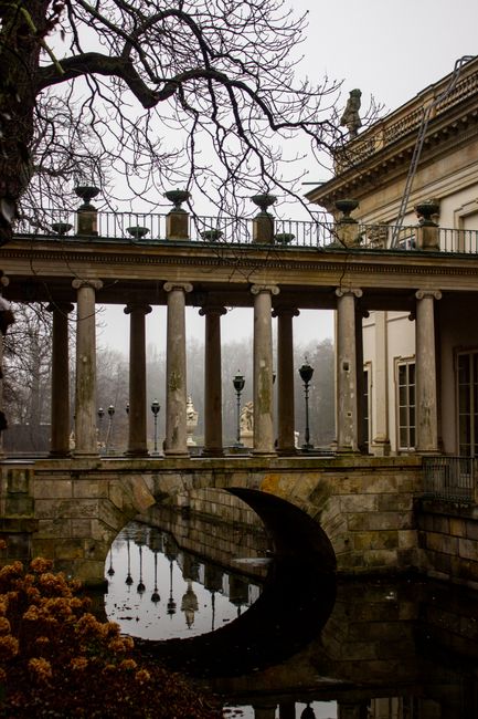 A classical stone bridge with columns in a misty park setting during winter.