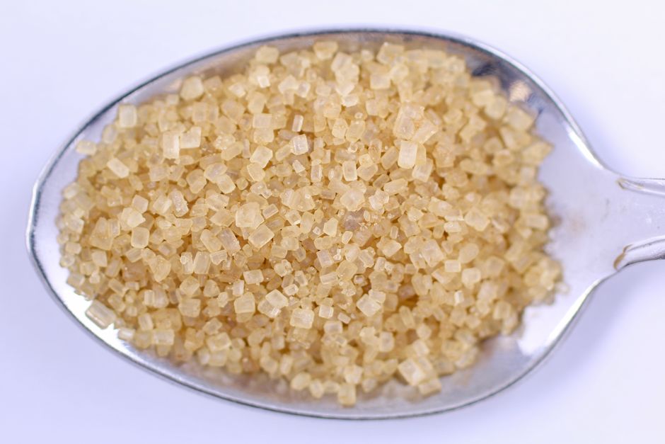 Detailed close-up of raw brown sugar on a metal spoon, perfect for food and cooking themes.