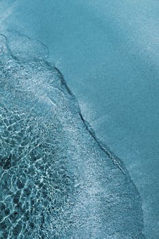 从空中俯瞰，蔚蓝的海洋与沙质海岸线宁静而美丽，展现了大自然的壮丽