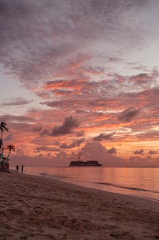 Stunning sunset view of a cruise ship near a Caribbean beach with vivid skies.