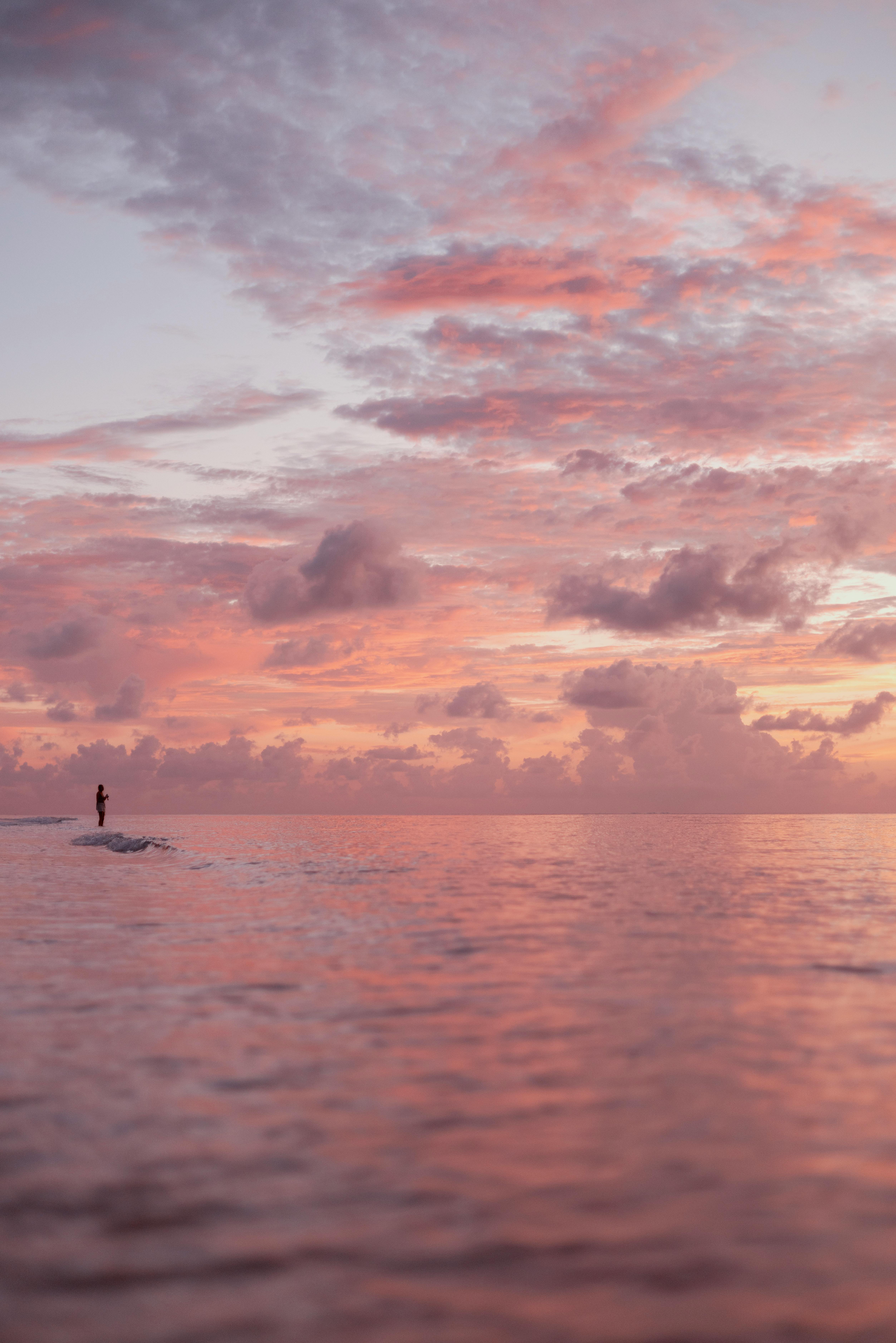 A lone figure stands in the ocean with a stunning sunset sky in the Cayman Islands.